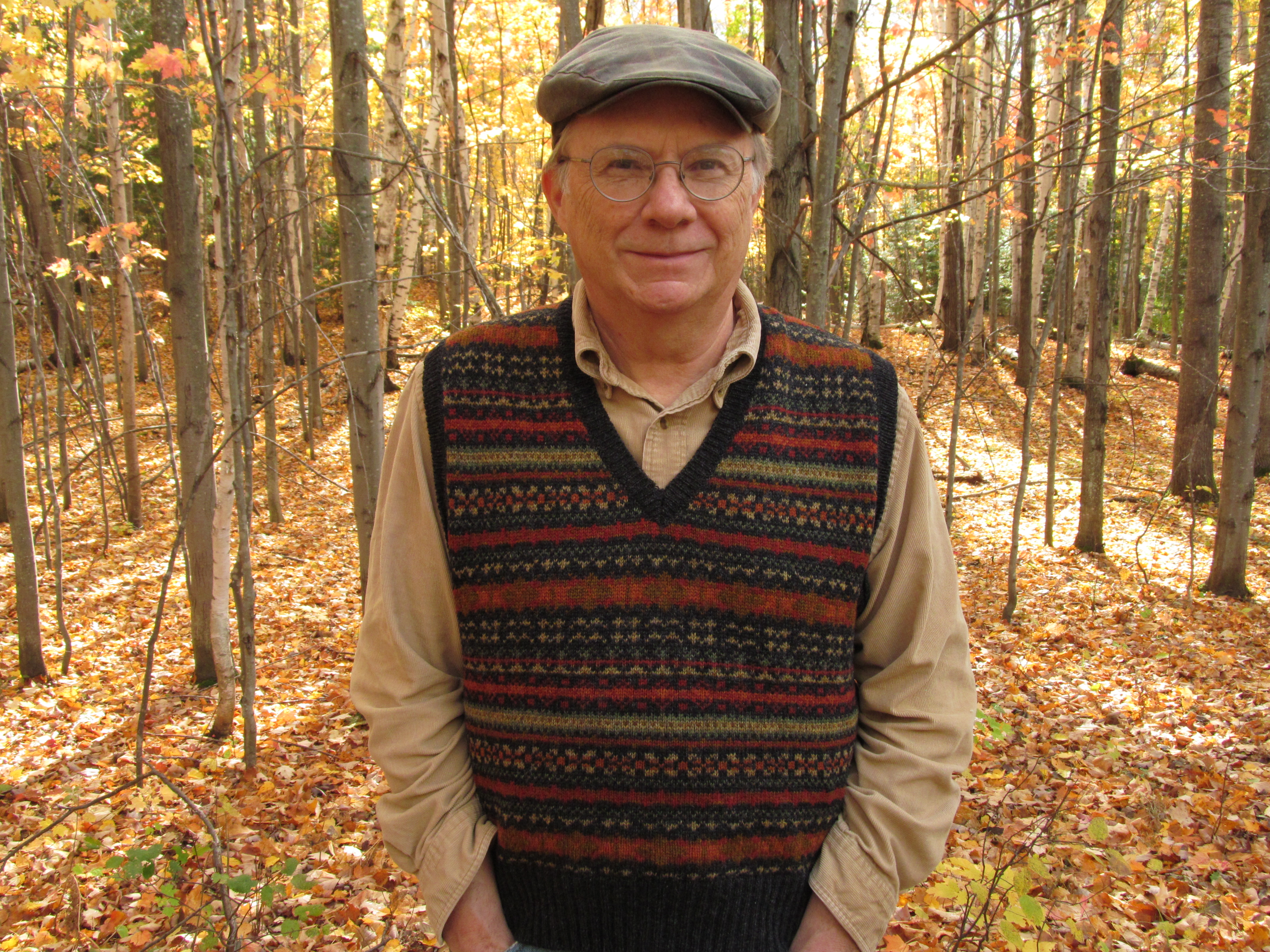 Russell Thorburn in autumn woods, wearing a Fair Isle vest and flat cap.